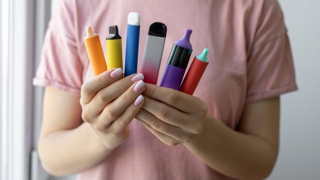 Person holding colorful vape pens in hands.